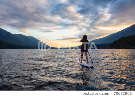 Woman Paddleboarding on Scenic Lake at Sunset 70672906