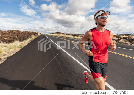 Runner fit athlete man running in triathlon suit training for Iron man on Hawaii. Fit male triathlete exercising endurance cardio on road 70675091