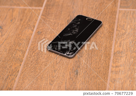 A broken phone is on the floor. Smartphone cracked screen closeup. A broken phone is on the floor. Smartphone cracked screen closeup. 70677229