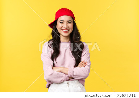 People emotions, lifestyle leisure and beauty concept. Happy cheerful asian woman smiling and laughing, cross arms chest, looking cool in hipster red cap over yellow background People emotions, lifestyle leisure and beauty concept. Happy cheerful asian woman smiling and laughing, cross arms chest, looking cool in hipster red cap over yellow background 70677311