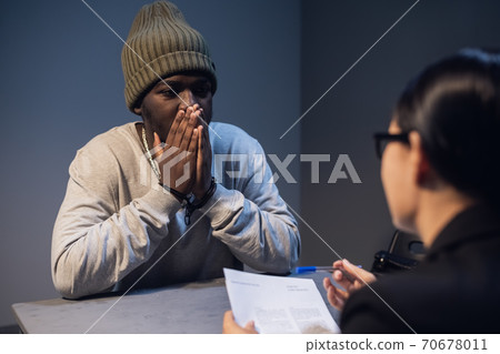 A black criminal in a hat communicates with his lawyer at the table in the police station 70678011