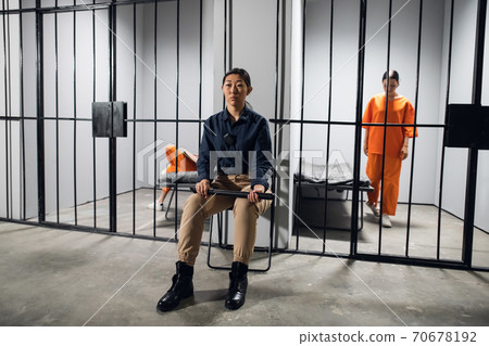 A young asian woman in uniform guards two criminals in prison 70678192