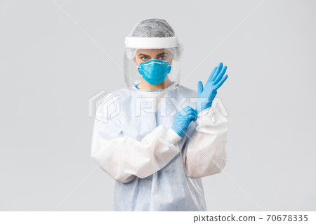 Covid-19, preventing virus, health, healthcare workers and quarantine concept. Serious female doctor in personal protective equipment PPE, shield, face mask out on gloves to enter patient room Covid-19, preventing virus, health, healthcare workers and quarantine concept. Serious female doctor in personal protective equipment PPE, shield, face mask out on gloves to enter patient room 70678335