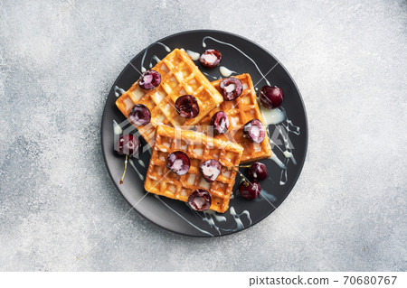 Belgian fluted waffles with fresh cherries and cream on a plate. Soft homemade waffles, sweet dessert with cherries. copy space 70680767