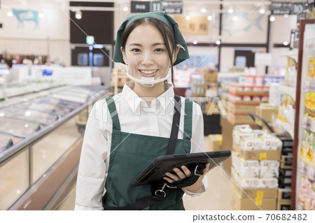 A female employee looking at a camera with a mouse shield that manages inventory at a supermarket A female employee looking at a camera with a mouse shield that manages inventory at a supermarket 70682482