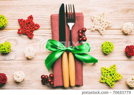 Top view of holiday set of fork and knife on wooden background. Close up of Christmas decorations and toys. New Year Eve concept Top view of holiday set of fork and knife on wooden background. Close up of Christmas decorations and toys. New Year Eve concept 70683779