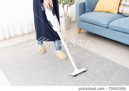 Young woman cleaning the living room with a cordless vacuum cleaner 70683986