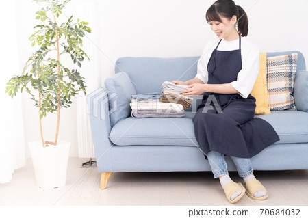 年輕女子坐在沙發上,折疊洗衣 年輕女子坐在沙發上,折疊洗衣 70684032