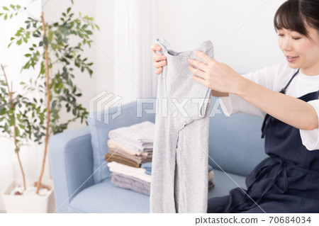 Young woman sitting on the couch and folding the laundry Young woman sitting on the couch and folding the laundry 70684034