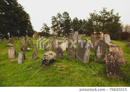 Old ancient Jewish cemetery historical place in Miory, Vitebsk region, Belarus. Mystical atmosphere, monuments covered by moss, green grass and yellow red autumn leaves, heavy grey sky 70685015