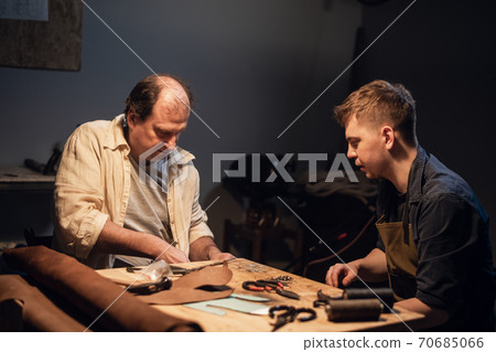 an experienced shoemaker and his assistant in their workshop make shoes from leather to order. an experienced shoemaker and his assistant in their workshop make shoes from leather to order. 70685066