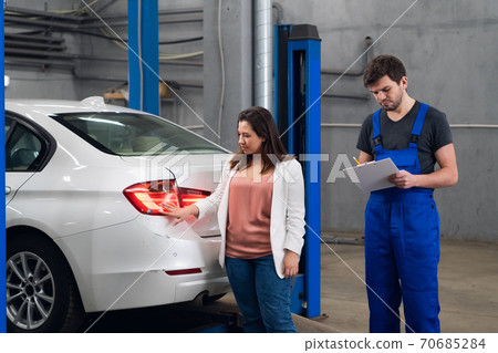 A man in a car service tells a customer about a repair 70685284