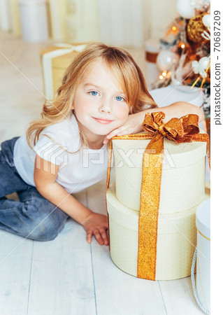 Little girl with gift box near Christmas tree on Christmas eve at home. Young kid in light room with winter decoration. Happy family at home. Christmas New Year december time for celebration concept Little girl with gift box near Christmas tree on Christmas eve at home. Young kid in light room with winter decoration. Happy family at home. Christmas New Year december time for celebration concept 70687209