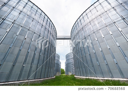 Agricultural Silos. Building Exterior. Storage and drying of grains, wheat, corn, soy, sunflower against the blue sky with white clouds Agricultural Silos. Building Exterior. Storage and drying of grains, wheat, corn, soy, sunflower against the blue sky with white clouds 70688568