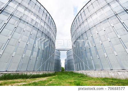 Agricultural Silos. Building Exterior. Storage and drying of grains, wheat, corn, soy, sunflower against the blue sky with white clouds Agricultural Silos. Building Exterior. Storage and drying of grains, wheat, corn, soy, sunflower against the blue sky with white clouds 70688577
