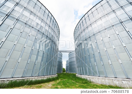 Agricultural Silos. Building Exterior. Storage and drying of grains, wheat, corn, soy, sunflower against the blue sky with white clouds Agricultural Silos. Building Exterior. Storage and drying of grains, wheat, corn, soy, sunflower against the blue sky with white clouds 70688578