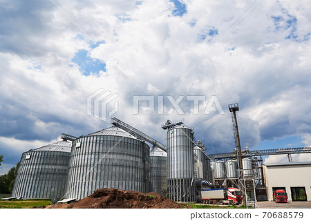 Agricultural Silos. Building Exterior. Storage and drying of grains, wheat, corn, soy, sunflower against the blue sky with white clouds 70688579