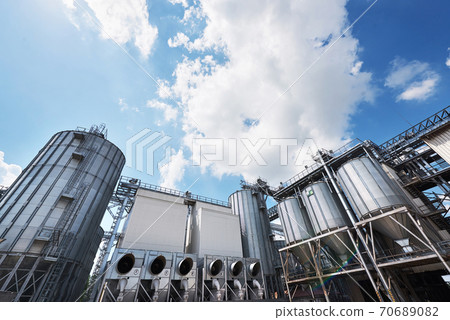 Agricultural Silos. Building Exterior. Storage and drying of grains, wheat, corn, soy, sunflower against the blue sky with white clouds Agricultural Silos. Building Exterior. Storage and drying of grains, wheat, corn, soy, sunflower against the blue sky with white clouds 70689082