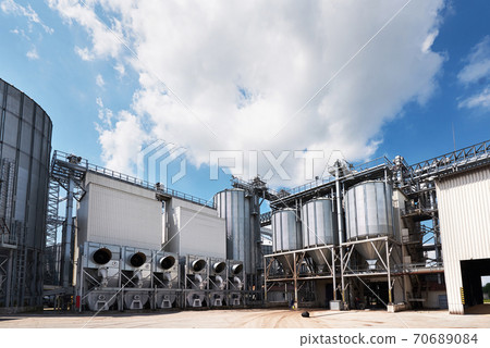Agricultural Silos. Building Exterior. Storage and drying of grains, wheat, corn, soy, sunflower against the blue sky with white clouds Agricultural Silos. Building Exterior. Storage and drying of grains, wheat, corn, soy, sunflower against the blue sky with white clouds 70689084
