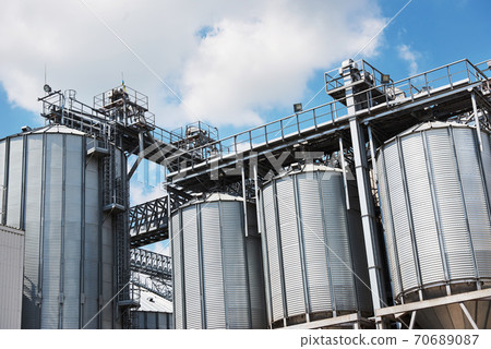 Agricultural Silos. Building Exterior. Storage and drying of grains, wheat, corn, soy, sunflower against the blue sky with white clouds Agricultural Silos. Building Exterior. Storage and drying of grains, wheat, corn, soy, sunflower against the blue sky with white clouds 70689087