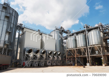 Agricultural Silos. Building Exterior. Storage and drying of grains, wheat, corn, soy, sunflower against the blue sky with white clouds Agricultural Silos. Building Exterior. Storage and drying of grains, wheat, corn, soy, sunflower against the blue sky with white clouds 70689090