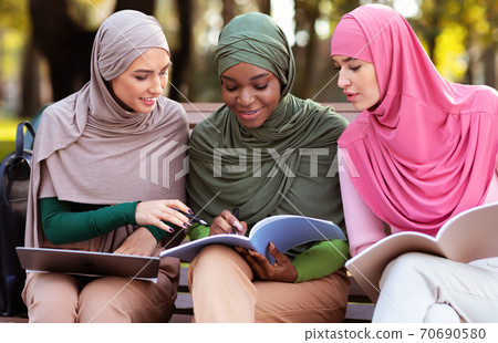 Three Female Arab Students Learning Together Reading Books Sitting Outdoors Three Female Arab Students Learning Together Reading Books Sitting Outdoors 70690580