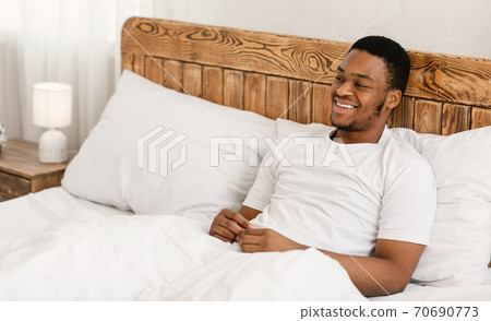 Happy Relaxed African American Man Sitting In Bed In Bedroom Happy Relaxed African American Man Sitting In Bed In Bedroom 70690773