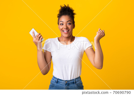 Excited afro lady feeling ecstatic holding smartphone Excited afro lady feeling ecstatic holding smartphone 70690790
