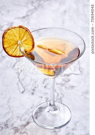 Martinez cocktail with dried orange slice and cedar. Yellow drink in martini glass on white marble 70694048