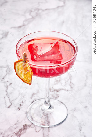 red cocktail with big piece of ice decorated with dried slice of orange. Copy space 70694049