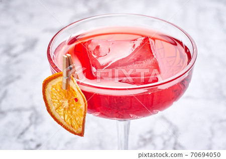 red cocktail with big piece of ice decorated with dried slice of orange. Copy space 70694050