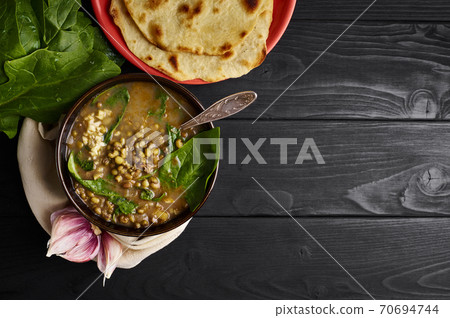 Spinach Mung Dhal and Chapati on black wooden table top. Moong Dal - Indian Cuisine curry. Spinach Mung Dhal and Chapati on black wooden table top. Moong Dal - Indian Cuisine curry. 70694744