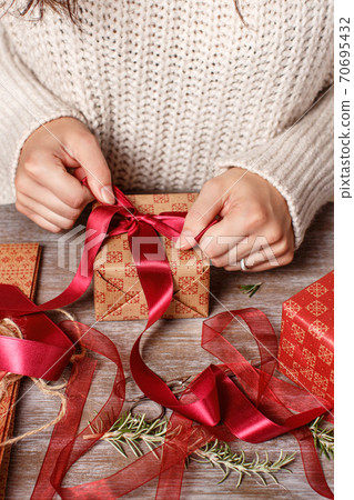 Woman ties a ribbon bow and wrapping presents Woman ties a ribbon bow and wrapping presents 70695432