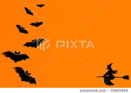 Silhouettes of a flock of bats and a witch flying on a broom made of black paper on an orange Silhouettes of a flock of bats and a witch flying on a broom made of black paper on an orange 70695969