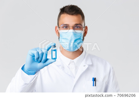 Covid-19, healthcare workers, pandemic and preventing virus concept. Smiling hispanic doctor, physician in medical mask and rubber gloves, showing ampoule with coronavirus vaccine, tell to vaccinate Covid-19, healthcare workers, pandemic and preventing virus concept. Smiling hispanic doctor, physician in medical mask and rubber gloves, showing ampoule with coronavirus vaccine, tell to vaccinate 70696206