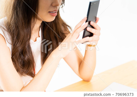 A woman operating a smartphone at a table [Parts cut] 70696373