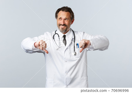 Covid-19, coronavirus outbreak, healthcare workers and pandemic concept. Skeptical and reluctant male doctor in white coat look away grimacing displeased, show thumbs-down 70696996