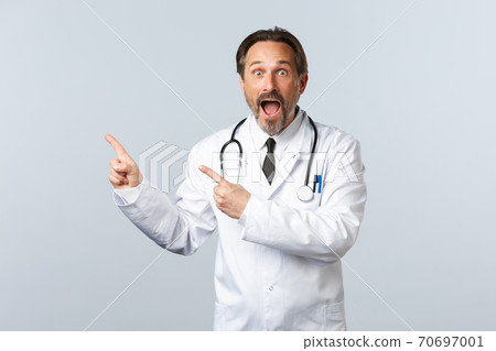 Covid-19, coronavirus outbreak, healthcare workers and pandemic concept. Excited and amazed gasping male doctor, drop jaw and staring camera as pointing upper left corner at banner Covid-19, coronavirus outbreak, healthcare workers and pandemic concept. Excited and amazed gasping male doctor, drop jaw and staring camera as pointing upper left corner at banner 70697001