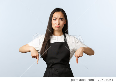 Coffee shop, small business and startup concept. Disappointed and upset cute asian female cafe waitress or barista in black apron, sulking and frowning displeased, pointing fingers down Coffee shop, small business and startup concept. Disappointed and upset cute asian female cafe waitress or barista in black apron, sulking and frowning displeased, pointing fingers down 70697064