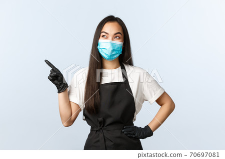 Covid-19 pandemic, social distancing, small business and preventing virus concept. Pleased smiling asian female coffee shop barista in medical mask and gloves seeing good promo at upper left corner Covid-19 pandemic, social distancing, small business and preventing virus concept. Pleased smiling asian female coffee shop barista in medical mask and gloves seeing good promo at upper left corner 70697081