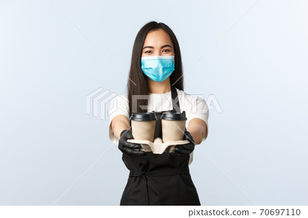 Covid-19, social distancing, small coffee shop business and preventing virus concept. Friendly pleasant asian waitress, cafe barista in medical mask serving coffee, handing order with takeaway cups 70697110