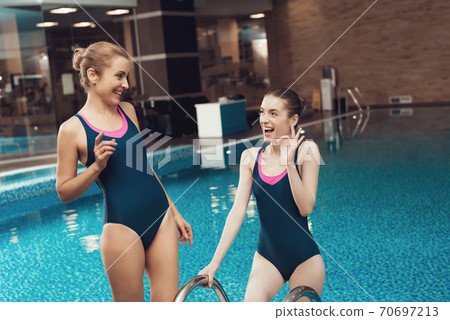 Two women standing near the pool at the gym.  70697213