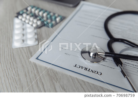 Modern doctor's office desk. Stethoscope and healthcare contract on wooden table close-up Modern doctor's office desk. Stethoscope and healthcare contract on wooden table close-up 70698759
