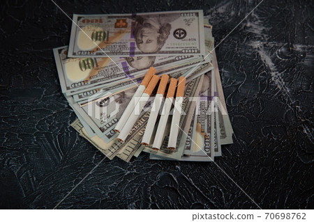 Dollar banknotes and cigarettes on grey background. Expensive and dangerous habit Dollar banknotes and cigarettes on grey background. Expensive and dangerous habit 70698762
