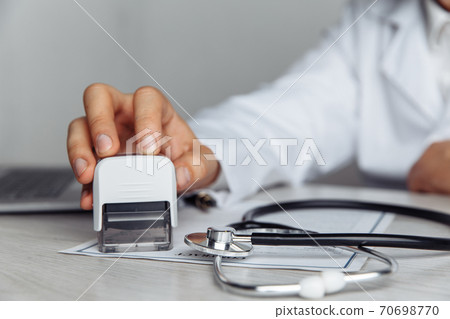 Male doctor in office is stamping medical document. Close-up hand. Medicine and healthcare concept Male doctor in office is stamping medical document. Close-up hand. Medicine and healthcare concept 70698770