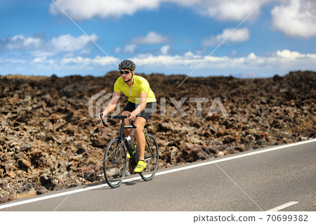 Triathlon biking cyclist man athlete on road bike. Fitness workout outdoors in nature landscape. Male sports competition. 70699382