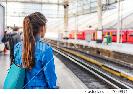 Train station morning commute woman going to work waiting for train to arrive. People on public transport platform . Commuting on rush hour. View of businesspeople and rails city lifestyle. 70699941