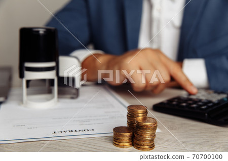 Man is counting profit on a calculator, stack of coins on desk in office. Economy and management financial concept 70700100