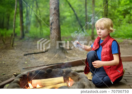 Little boy during family hiking plays with a burning stick by bonfire. Child having fun at camp fire Little boy during family hiking plays with a burning stick by bonfire. Child having fun at camp fire 70700750