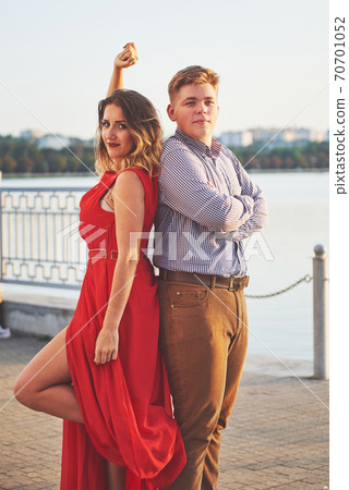 Happy beautiful woman in red dress and young man dance of on summer with lake in the background. Color contrast red and white Happy beautiful woman in red dress and young man dance of on summer with lake in the background. Color contrast red and white 70701052